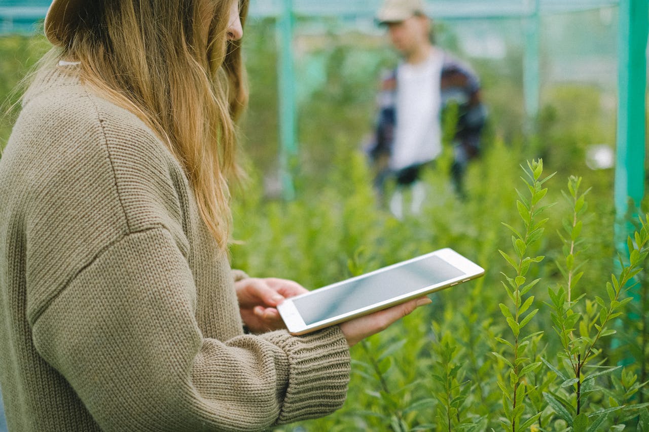 A woman using a tablet in a greenhouse for managing plant growth, indicating technology in agriculture.